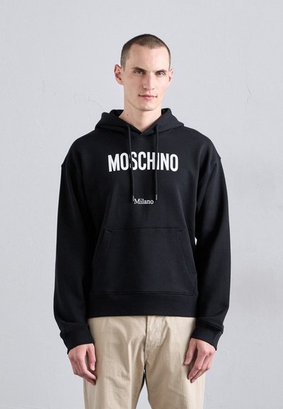 Felpa nera Moschino con logo bianco e testo "Milano", dotata di tasca frontale e cappuccio regolabile con cordino. Tessuto morbido e texture.