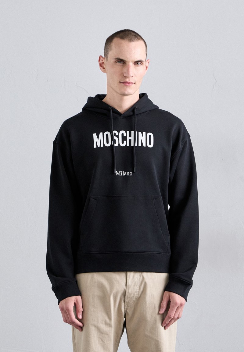 Hanorac negru Moschino cu logo alb și text "Milano", având o buzunar frontal și glugă cu șnur ajustabil. Material moale, texturat.