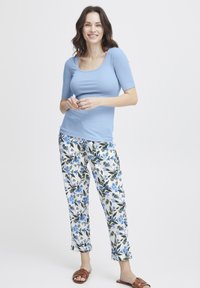 Lichtblauw T-shirt met korte mouwen gecombineerd met witte broek met een blauw bloemmotief. Bruine slippers maken de outfit compleet.