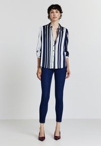 Marineblau-weiß gestreifte Bluse mit Knöpfen; lange Ärmel hochgekrempelt. Kombiniert mit dunkelblauen Skinny Jeans und bordeauxroten spitzen Absätzen.