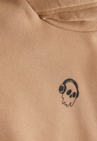 Beige sweatshirtstof med en blød tekstur med en sort grafik af en dryppende kranie med hovedtelefoner på venstre brystområde.