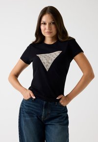 Must mustreid mustärge valmistatud tees, millel on ees kolmnurkne beež mustriga aksent. Ümmargune krae disain, lühikesed varrukad, kombineeritud teksapükstega.