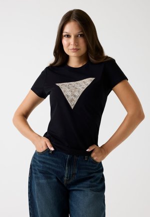 Must mustreid mustärge valmistatud tees, millel on ees kolmnurkne beež mustriga aksent. Ümmargune krae disain, lühikesed varrukad, kombineeritud teksapükstega.