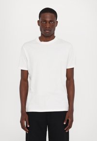 T-shirt blanc à manches courtes en coton, avec un col rond et un petit logo gris clair sur le côté gauche de la poitrine. Design simple.