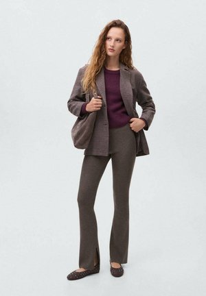 Een bruine geruite blazer over een bordeauxrode trui, gecombineerd met aansluitende bruine geribbelde broeken met zijspleten, en bruin instap schoenen met studs.