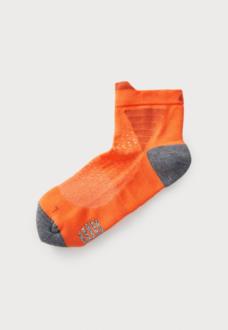Calcetín deportivo naranja con un talón y puntera grises, que presenta patrones texturizados y agujeros de ventilación en los laterales para mayor transpirabilidad.