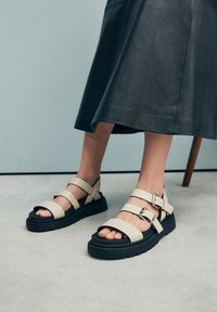 Beige plateau sandalen met verstelbare bandjes, zwarte rubberen zolen en metalen gespen. Het ontwerp heeft meerdere bandjes over de voet.