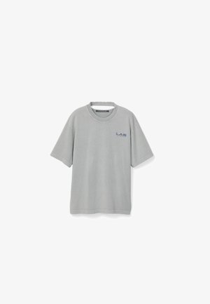 T-shirt gris clair à manches courtes col rond avec petit logo bleu "LAB" sur la poitrine gauche et étiquette "CAMPERLAB" à l'intérieur du col.