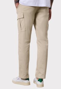 Beige cargo kalhoty s dvěma bočními kapsami, rovnými nohavicemi a směsí bavlny, kombinované s bílými teniskami a zelenými akcenty.