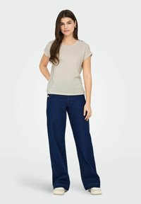 Beige gestreiftes kurzärmliges T-Shirt, kombiniert mit dunkelblauen weiten Jeans. Das T-Shirt hat einen Rundhalsausschnitt; die Jeans verfügen über ein Knopfdetail.