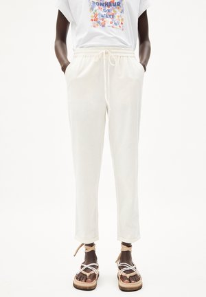 Personne portant un pantalon blanc à cordon, un t-shirt graphique blanc avec un imprimé coloré, et des sandales à plateforme beige avec des sangles.