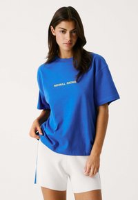 Zila kokvilnas t-kreklu ar īsām piedurknēm un apaļu izgriezumu, ar dzeltenu uzrakstu "RED BULL RACING" uz priekšpuses.