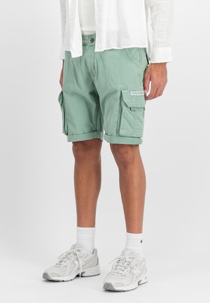 Mint green cargo shorts with rolled hems, multiple side pockets, made from lightweight fabric, paired with gray athletic shoes and white socks.