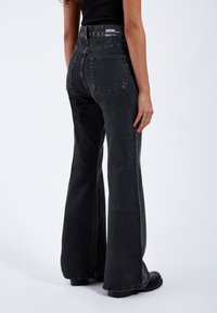 Flared black denim jeans with a high waist, two back pockets, and a generic brand tag at the waist. Soft texture, minimal distressing.