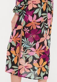 Robe fleurie en tissu léger, avec des fleurs roses, orange et violettes vibrantes sur un fond noir. Détail d'une fente sur le côté visible.