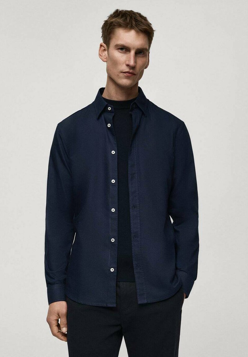 Camicia blusa navy con colletto, maniche lunghe e una texture liscia. Presenta bottoni bianchi e una vestibilità rilassata.