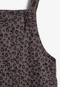 Olifantenprint tuinbroeken in bruin en zwart. Textuur stof met zwarte olifantenvlekken en een strikdetail op de bandjes. Bronzen knoop hardware.