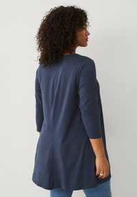 Marineblauwe, lange mouwen tuniek met een ronde halslijn, licht uitlopende vorm en zachte textuur. De achterkant heeft een subtiele naaddetails.