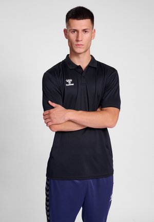 Zwarte polo met korte mouwen, heeft een kraag en een subtiele ribbelstructuur; logo op de linkerkant van de borst. Graagd met marineblauwe sportbroek.