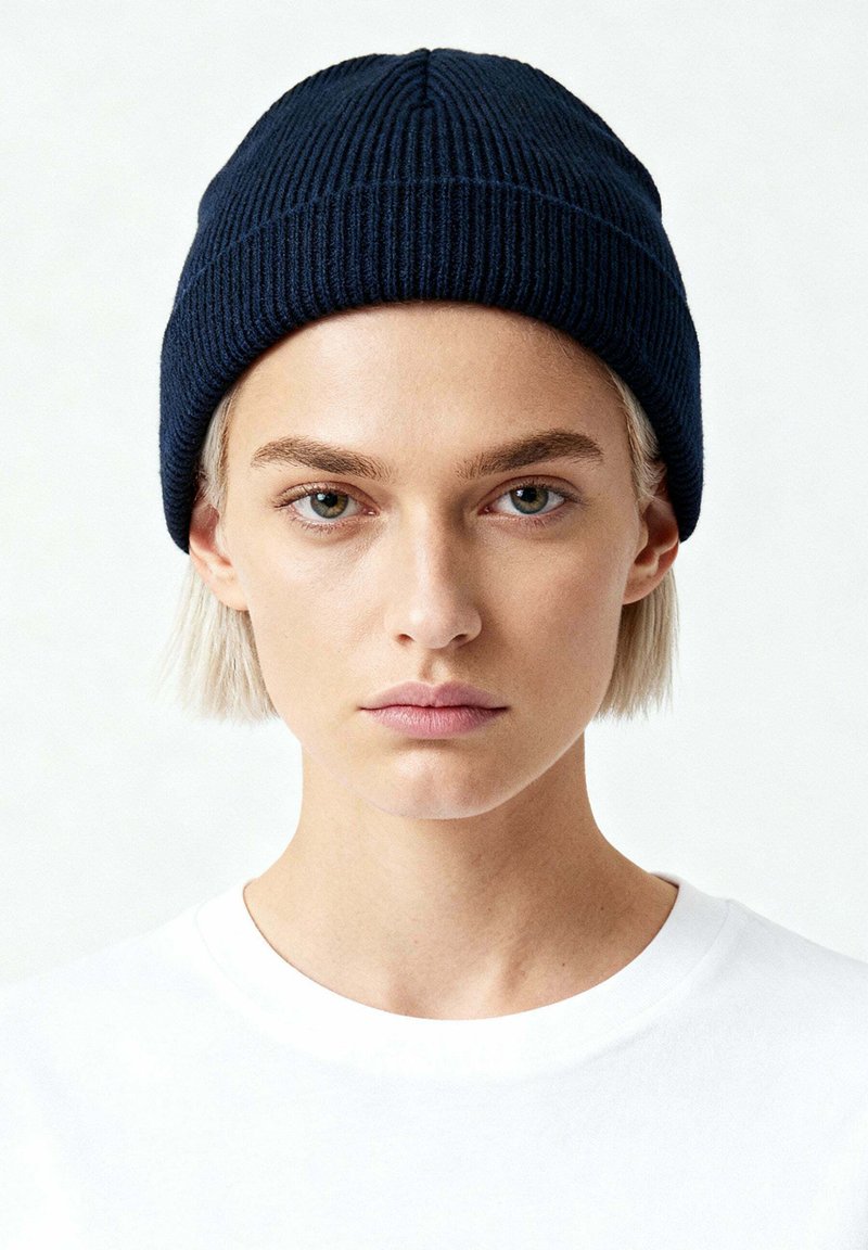 Cappello a cuffia in maglia a coste color blu navy con parte superiore arrotondata, caratterizzato da una texture verticale e un design semplice. Indossato sopra una t-shirt bianca semplice.