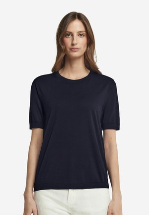 T-shirt navy a maniche corte in tessuto morbido, con collo a giro e maniche arrotolate, abbinato a pantaloni chiari.