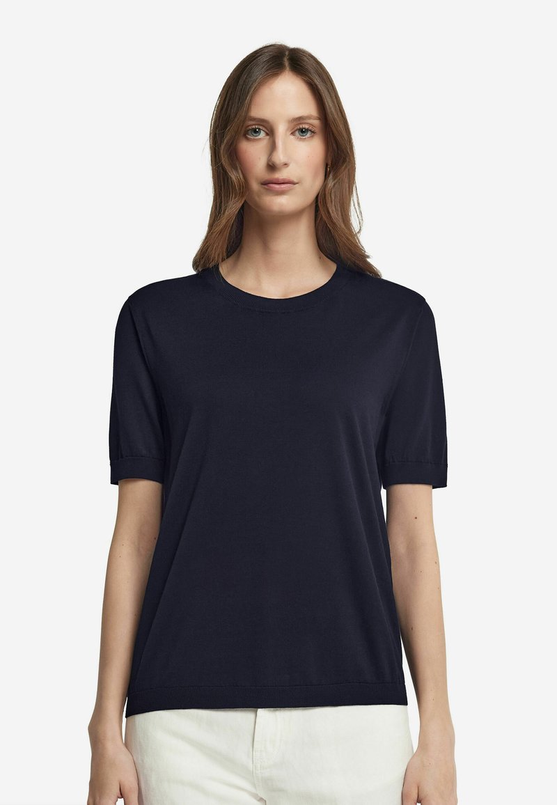 Marinblå kortärmad t-shirt i mjukt tyg, med rundad halsringning och uppvikta ärmar, kombinerad med ljusa byxor.