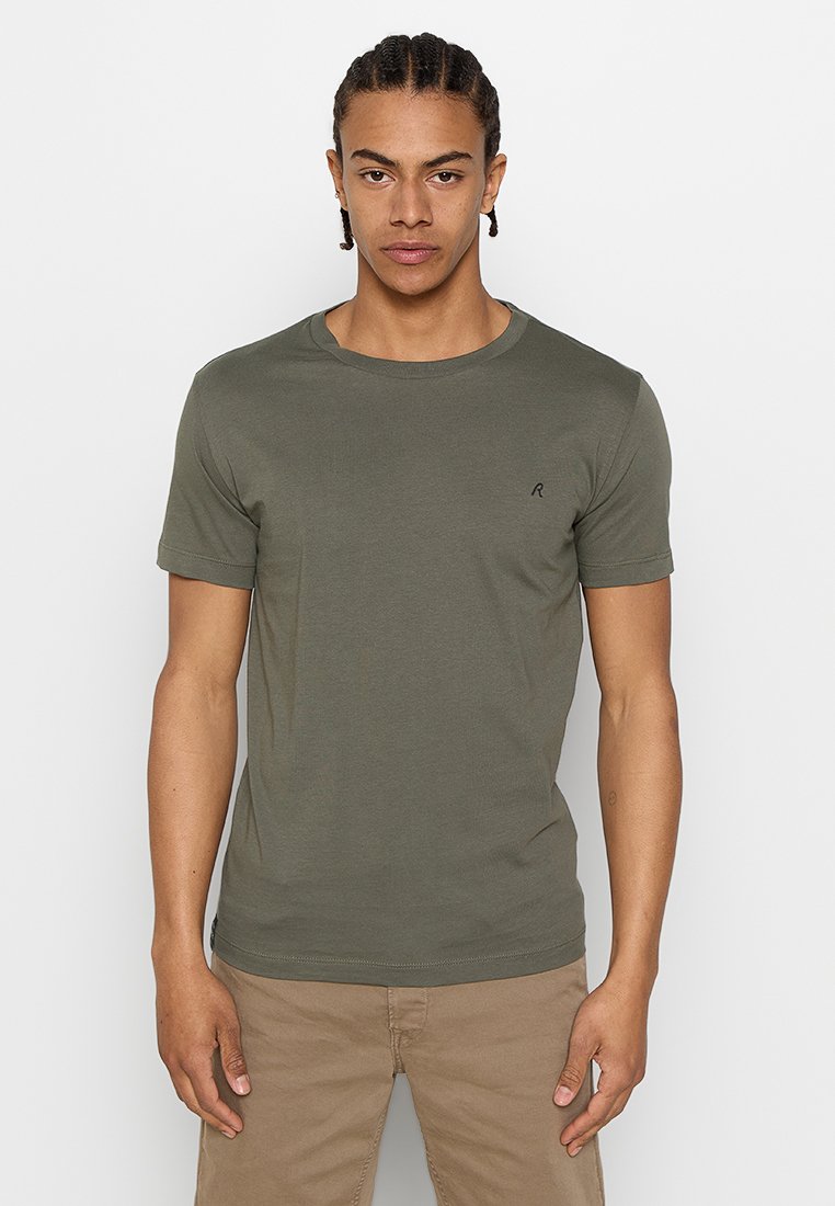 Camiseta de color verde oliva, de mangas cortas, con cuello redondo, hecha de una suave tela de algodón, presenta un pequeño logo negro en el pecho.