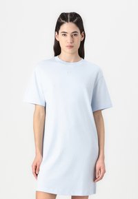 Svetlo modra oversize bombažna obleka s kratkimi rokavi in okroglo izrezom, ki ima na prsih majhen izšit Nike logotip.