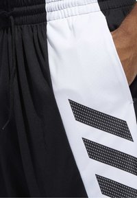 Schwarz-weiße Sportshorts aus leichtem Material, mit einem strukturierten weißen Einsatz mit schwarzen Chevron-Mustern und einem Kordelzugbund.