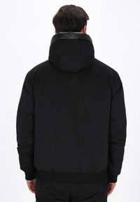 Sort isoleret bomberjakke med hætte, ribbede manchetter og talje. Har en glat tekstur og minimalistisk design.