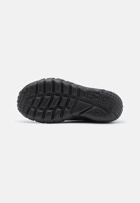 Semelle en caoutchouc noir avec texture, présentant un motif de gomme pour l'adhérence, un design épuré et un logo bien en vue.