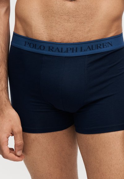 Αρσενικός κορμός με σκούρο μπλε boxer Polo Ralph Lauren με λογότυπο στη ζώνη, πάνω σε απλό φωτεινό φόντο.