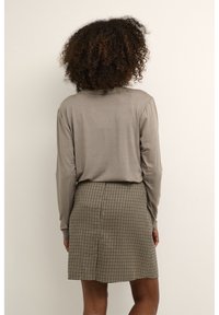 Maglia a maniche lunghe di colore marrone chiaro abbinata a una gonna corta a scacchi bianco e nero. Tessuto liscio; forma aderente. Vista posteriore.