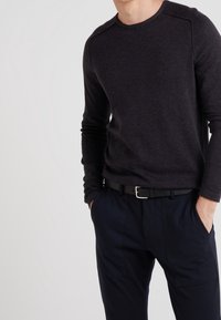 Maglia a maniche lunghe grigio scuro con scollo rotondo e cuciture sulle spalle. Abbinata a pantaloni blu navy, con cintura nera e fibbia argento.