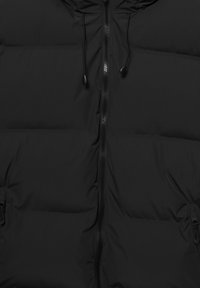 Črna puhovka z gladkim, mat zaključkom, navpičnim prešitim vzorcem, sprednjim zadrgo in kapuco z vrvico. Ima stranske žepe z zadrgami.