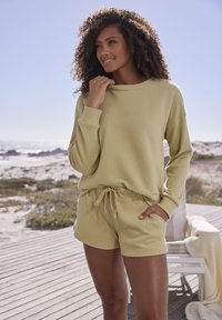 Hellgrüner Rippstrickpullover mit lockerer Passform, langen Ärmeln und hohem Kragen, kombiniert mit passenden Shorts mit Kordelzug, beide aus weichem Material.