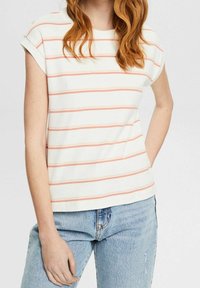 Gestreept T-shirt in het wit met koraalkleurige strepen, korte mouwen, ronde halslijn en zachte katoen; gecombineerd met lichtblauwe jeans.