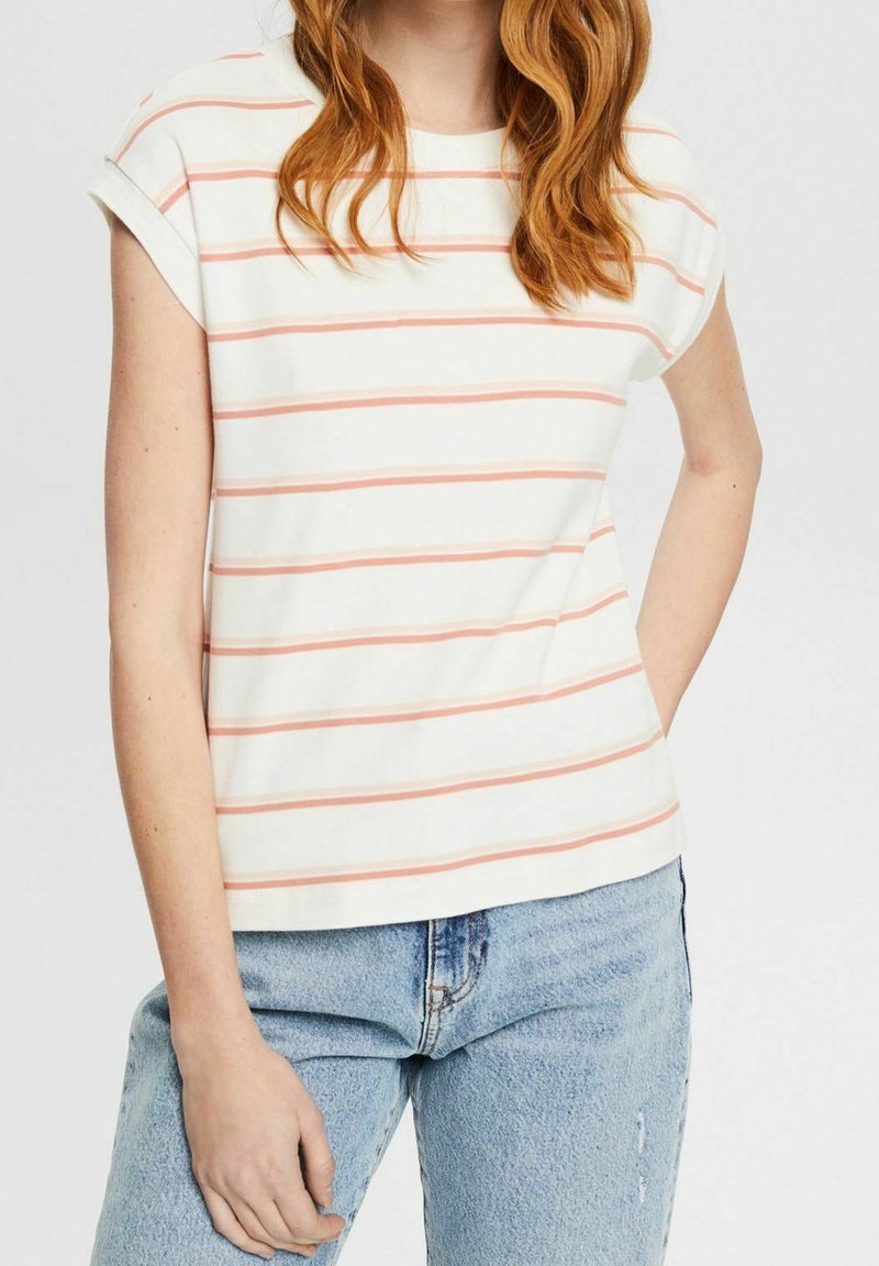 Gestreept T-shirt in het wit met koraalkleurige strepen, korte mouwen, ronde halslijn en zachte katoen; gecombineerd met lichtblauwe jeans.