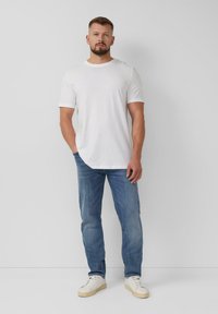 Biała koszulka z krótkim rękawem i okrągłym dekoltem, zestawiona z jasnoniebieskimi dżinsami i białymi trampkami. Slim fit, styl casualowy, minimalistyczny design.