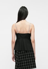 Czarny top peplum z cienkimi srebrnymi ramiączkami, gładką teksturą i wyraźnym kształtem, połączony z spódnicą w czarno-białą kratę.