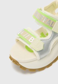 Hvit plattform sandal med sølvdetaljer, neongrønne stropper og en teksturert såle. Har justerbare stropper med "BUFFAL" merke.