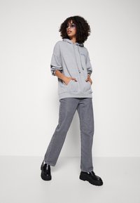 Sudadera gris con capucha y cordones, combinada con unos jeans gris de cintura alta y zapatos de plataforma negros. Tejido texturizado.
