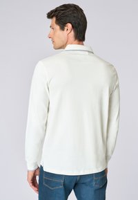 Polo shirt bianco a maniche lunghe con colletto, caratterizzato da un sottile accento blu sui bordi del colletto, abbinato a jeans in denim blu.