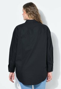 Camicia nera a maniche lunghe con colletto classico, dettagli sui polsini con bottone e orlo curvo, realizzata in tessuto liscio con una trama uniforme.