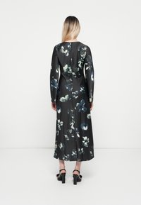 Long-sleeved black dress with a floral print in green and blue hues. Smooth fabric with a fitted silhouette and back slit detail.