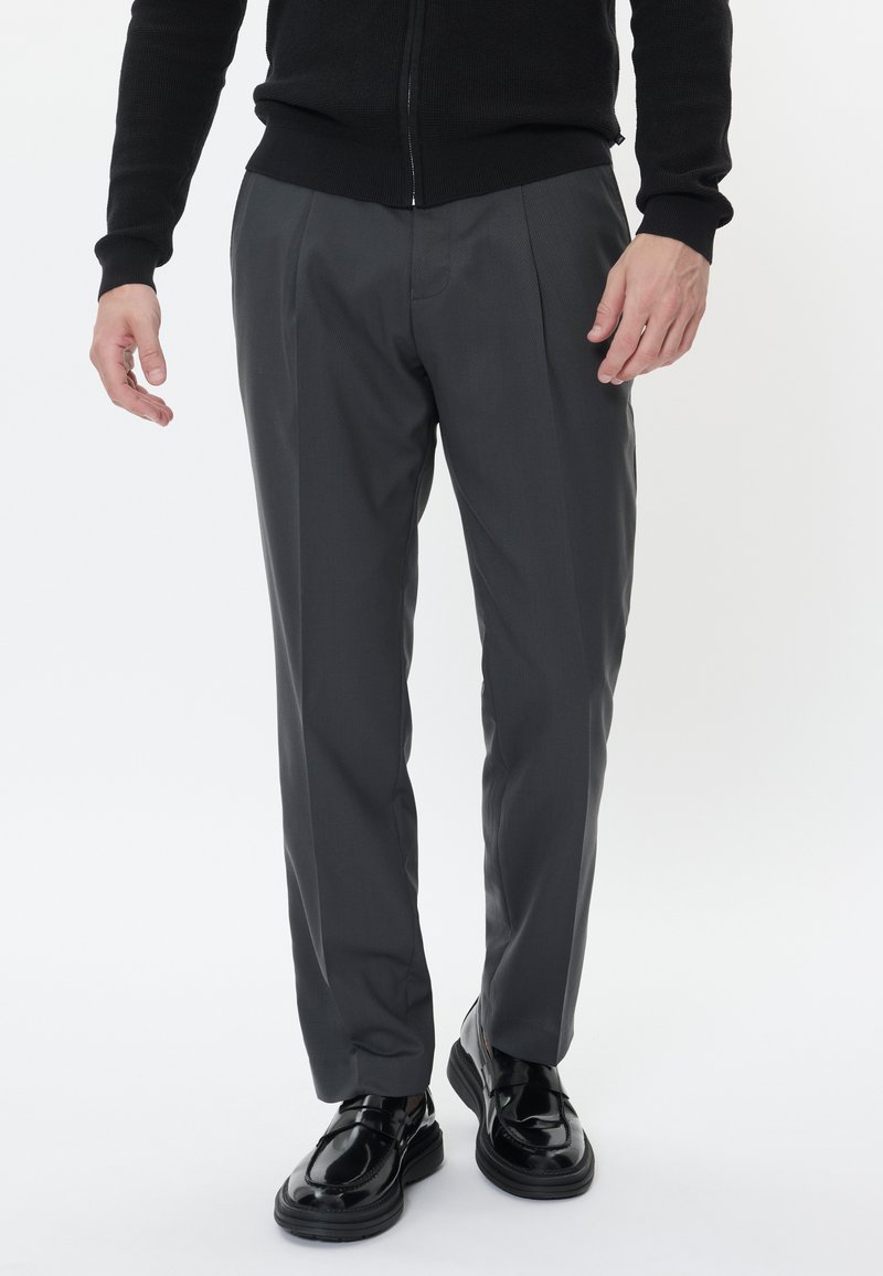 Šedé upravené kalhoty s hladkou texturou, zdobené předními sklady a úzkým střihem. V kombinaci s lesklými černými mokasíny.