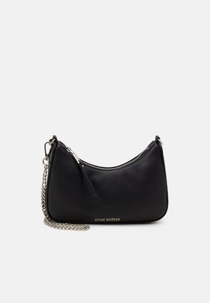 Czarna torebka Steve Madden z paskiem na łańcuchu w kolorze srebrnym i zamknięciem na zamek, na jednolitym jasnoszarym tle.
