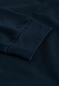 Dunkelblauer Stoff mit strukturierter Oberfläche, zeigt eine Nahaufnahme eines Ärmels mit glatter Verarbeitung und subtilen Nahtdetails.