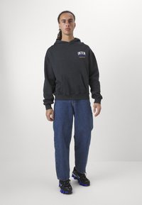 Hoodie preto com o texto "INTER" em amarelo, bolso frontal, combinado com jeans azuis e sapatilhas pretas com detalhes roxos.