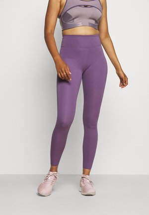 Legging taille haute violet en tissu extensible avec une texture douce, assorti à un soutien-gorge de sport et des baskets roses claires.